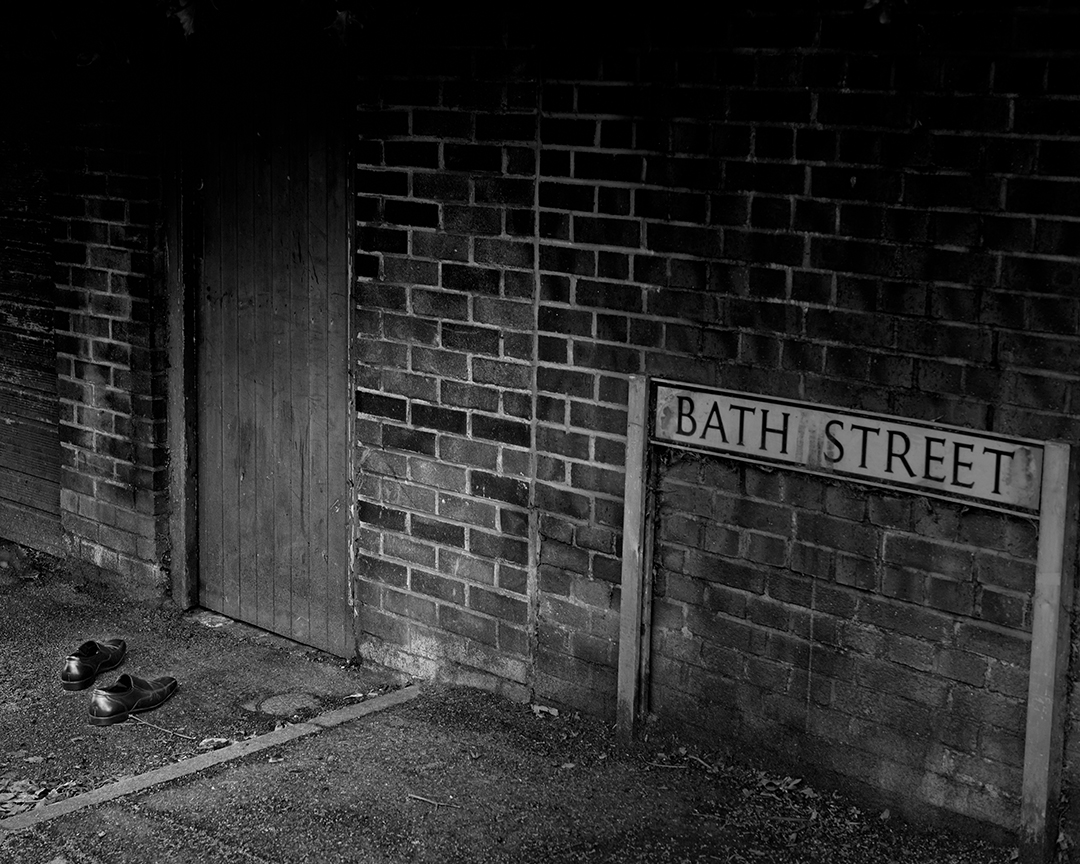 Black and white photograph of an empty pair of shoes on Bath Street beside a brick wall