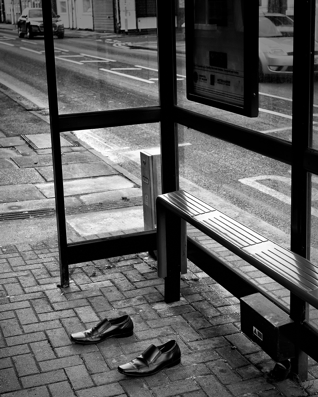 Black and white photograph of an empty pair of shoes at an empty bus shelter
