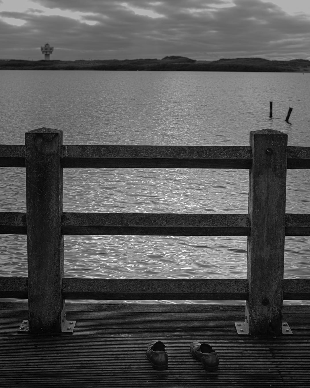 Black and white photograph of an empty pair of shoes left on a jetty overlooking water